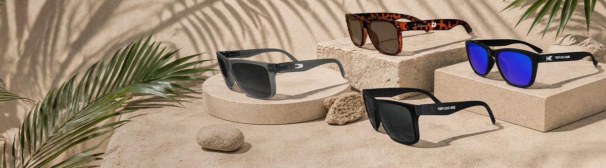 4 pairs of Knockaround customizable sunglasses photographed on sand/rock with plants. 