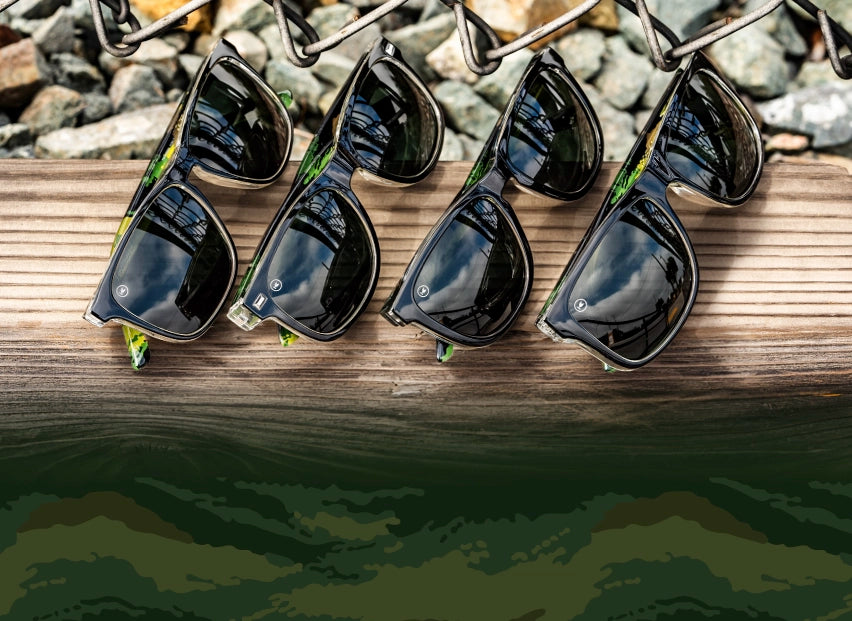 Covert Ops sunglasses. 4 pairs of black and camo print sunglasses with smoke lenses photographed on a wood in nature